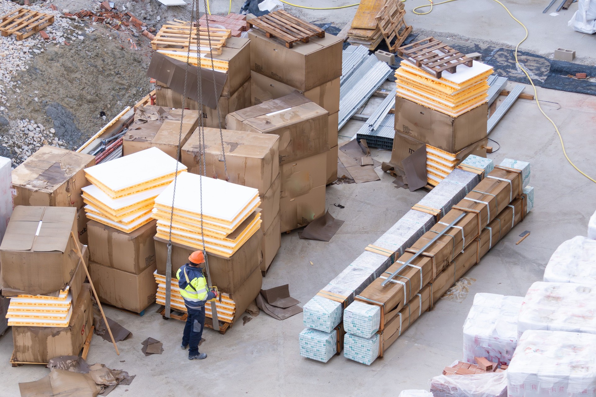 construction crane operator dressed in work clothes with yellow phosphorescent vest and orange hard hat. seen from above. ready to lift a load of construction material.