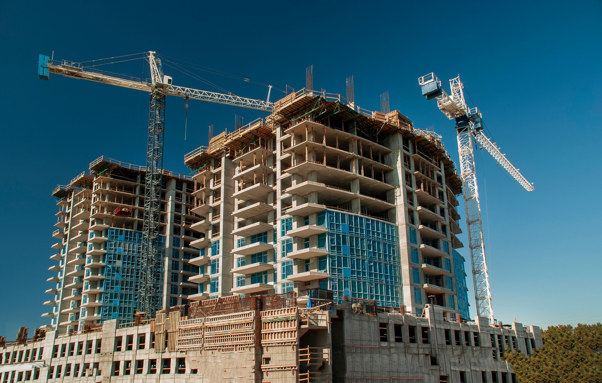 White crane towers at a large construction site with condominium balconies against a blue sky